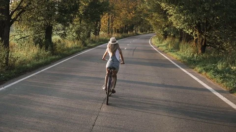 A young blonde girl in pants on retro bike going down the road in the field Stock Footage 81555152