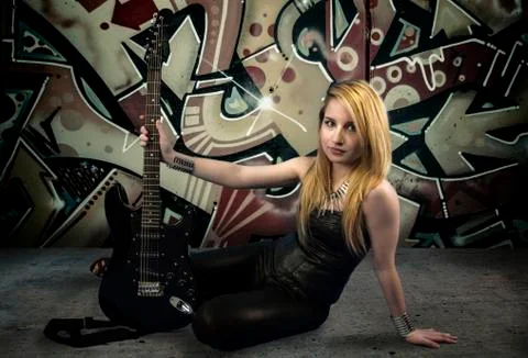 Young blonde holding a black guitar, over grafitti background Stock Photos