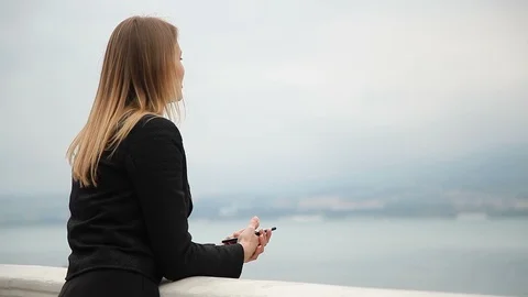 A young blonde leaned on the railing near the sea holding a phone Stock Footage 111925684