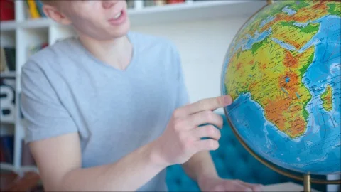 Young blonde man spinning the globe and looking for the island in the pacific Stock Footage 104425724