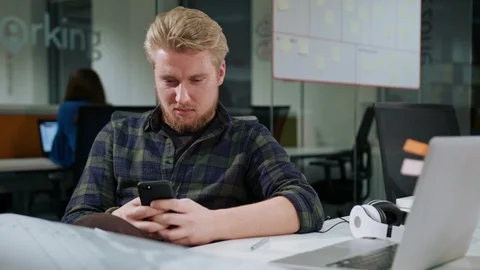 A Young Blonde Man Using a Phone in the Office Stock Footage 86351399