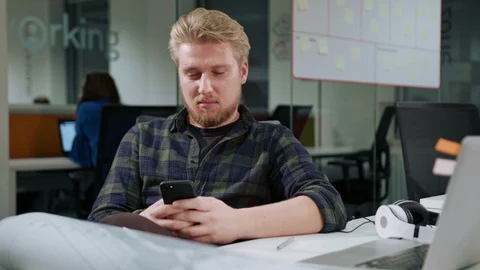 A Young Blonde Man Using a Phone in the Office Stock Footage 86351660