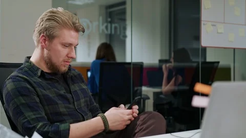 A Young Blonde Man Using a Phone in the Office Stock Footage 86358311