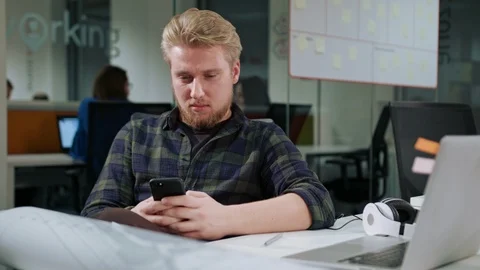 A Young Blonde Man Using a Phone in the Office Stock Footage 86359230
