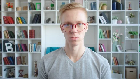 Young blonde map portrait wearing glasses. Shelves with books on the background Stock Footage 104453833