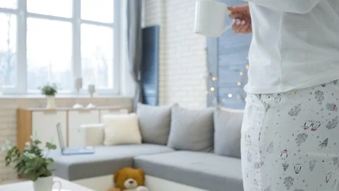 Young blonde puts the mug on the table and lay down on the sofa with a Video stock 102734852