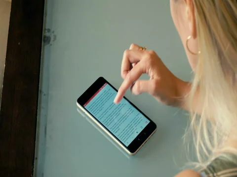 Young blonde reading an article in the phone while sitting at a table. Stock Footage 80562274