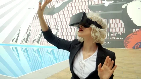 A young blonde is in a room for playing with virtual reality glasses 스톡 동영상 85991450