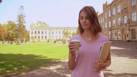 Young blonde student drinking coffee walking after class near university. girl Stock Footage 98486211