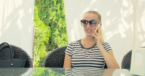 Young blonde talking on the smart-phone sitting on a chair in cafe. Stock Footage 80162928