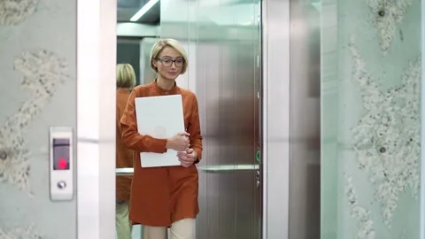 A young blonde woman exits the elevator of a modern office building. The lift  Stock Footage 239020751
