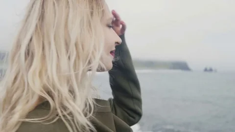 Young blonde woman standing on the beach, near the troll toes in Iceland, doing Stock Footage