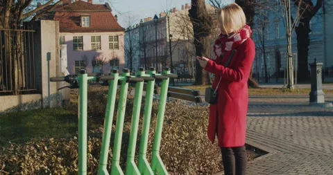 Young blonde woman using smartphone while unlocking green e-scooter on street Stock Footage 252139244