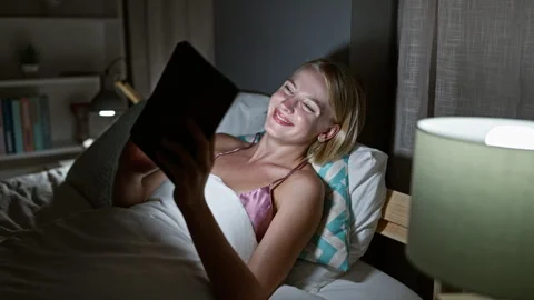Young blonde woman using touchpad lying on bed at bedroom Video stock 247379824