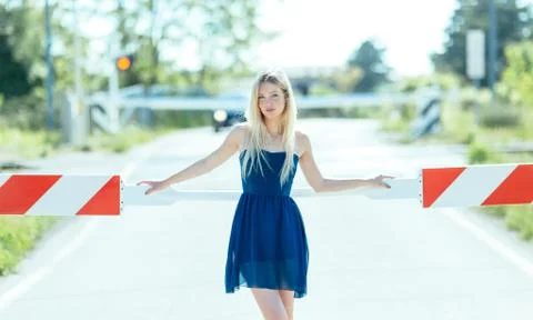 Young blonde woman waiting on automated level crossing with down barriers for Stock Photos
