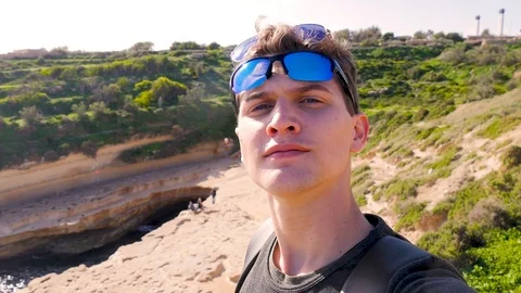 Young blue-eyed guy with two sunglasses makes a selfie against the backdrop of Stock Footage 101817849
