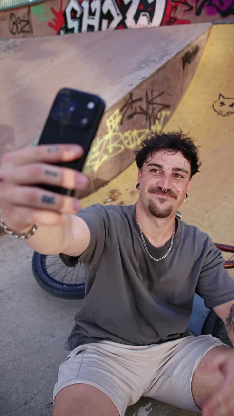 Young BMX rider taking selfie with smartphone in skatepark, smiling and making Stock Footage 336936504