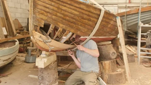 Young boat builder riveting planks on wooden lapstrake sailboat Stock Footage 338159251