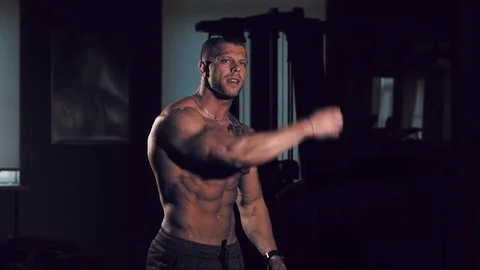 Young bodybuilder with a bare torso posing in a gym. 60 to 24fps 4K Stock Footage 74354645