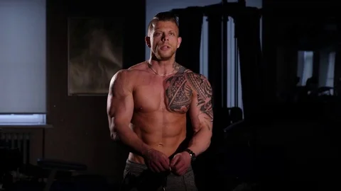 Young bodybuilder with a bare torso posing in a gym. 60 to 24fps 4K Stock Footage 74354992