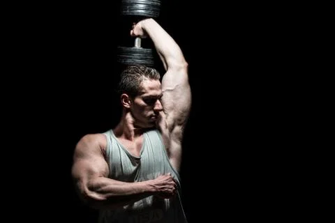 Young bodybuilder doing heavy weight exercise for shoulder on black backgroun Stock Photos