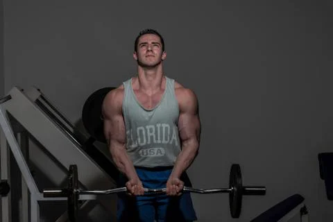 Young bodybuilder doing heavy weight exercise for biceps with barbell Stock Photos