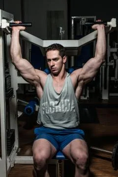 Young bodybuilder doing shoulder press on machine Stock Photos