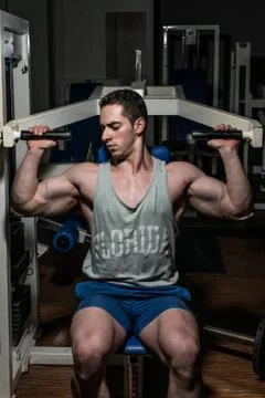 Young bodybuilder doing shoulder press on machine Stock Photos