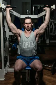 Young bodybuilder doing shoulder press on machine Stock Photos