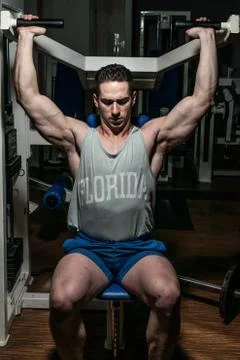Young bodybuilder doing shoulder press on machine Stock Photos