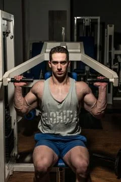 Young bodybuilder doing shoulder press on machine Stock Photos