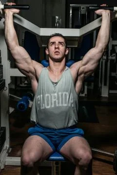 Young bodybuilder doing shoulder press on machine Stock Photos