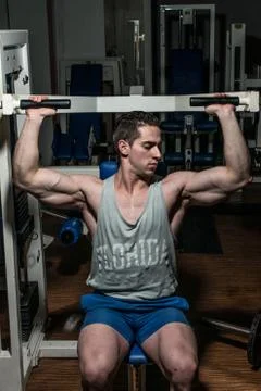 Young bodybuilder doing shoulder press on machine Stock Photos