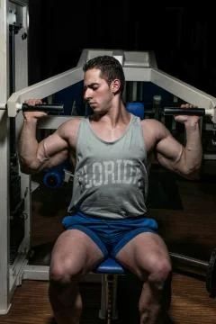 Young bodybuilder doing shoulder press on machine Stock Photos