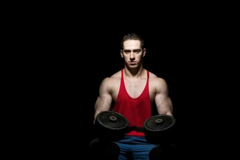Young bodybuilder posing with dumbbell at the bench on black background Stock Photos