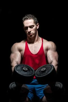 Young bodybuilder posing with dumbbell at the bench on black background Stock Photos