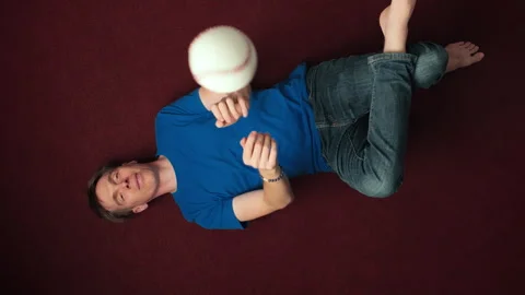 Young bored man lying on the floor and throwing a ball Vídeo Stock 342510949