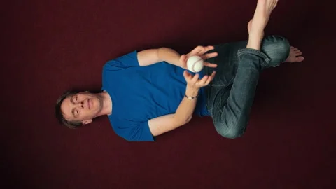 Young bored man lying on the floor and throwing a ball Vídeo Stock 342511842