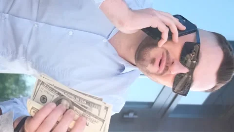 A young boss with dollars in his hands is talking on a smartphone. Vertical Stock Footage 250029629