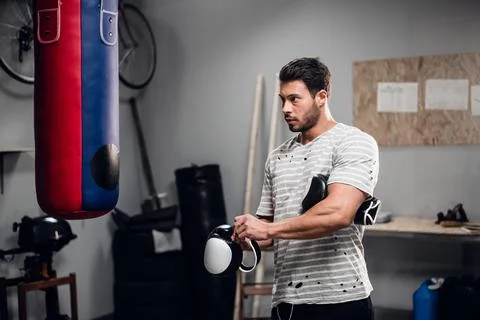 A young boxer prepares for training, puts on Boxing gloves in the gym. Stock Photos