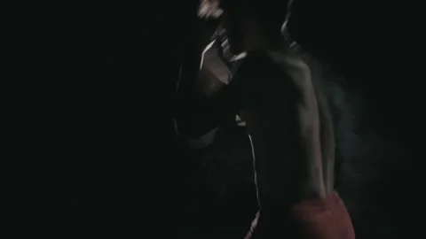 A young boxer trainings hard in a dark opposite a light Stock Footage 154699576