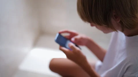 Young boy absorbed in smartphone while sitting on toilet, unable to disconn.. Stock Footage 340387554