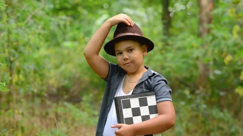 Young Boy Adjusting Hat and Holding Chessboard Smiling Outdoors Video stock 343550221