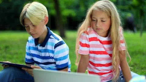 Young boy and girl using technology in summer green park. Kids use laptop and Видео 137859040