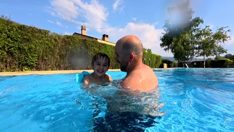 Young boy with arm bands jumping into father's arms in a swimming pool Stock Footage 336059456