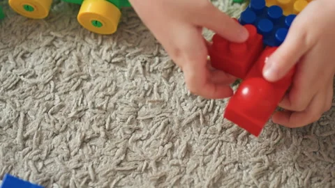 Young boy assembling vibrant car on carpet. Young boy concentrates while putting Stock Footage 337725815