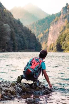 Young boy with backpack sitting on rock over a river Stock Photos