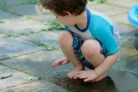 Young boy in a bathing suit playing in a puddle of water in the backyard ne.. Stock Photos