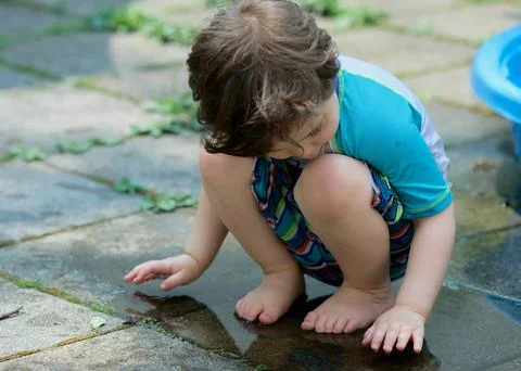 Young boy in a bathing suit playing in a puddle of water in the backyard ne.. 库存照片