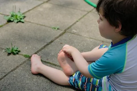 Young boy in a bathing suit twisting his feet on the ground Stock Photos